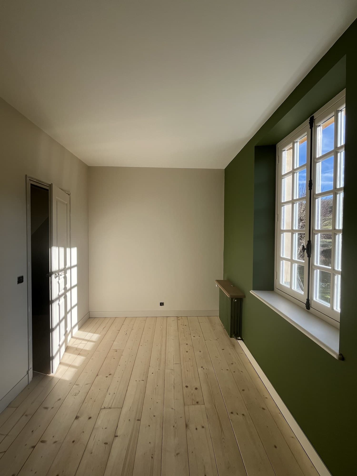 Pièce sous comble aux murs vert profond, deux fenêtres à petits bois et parquet pin clair
