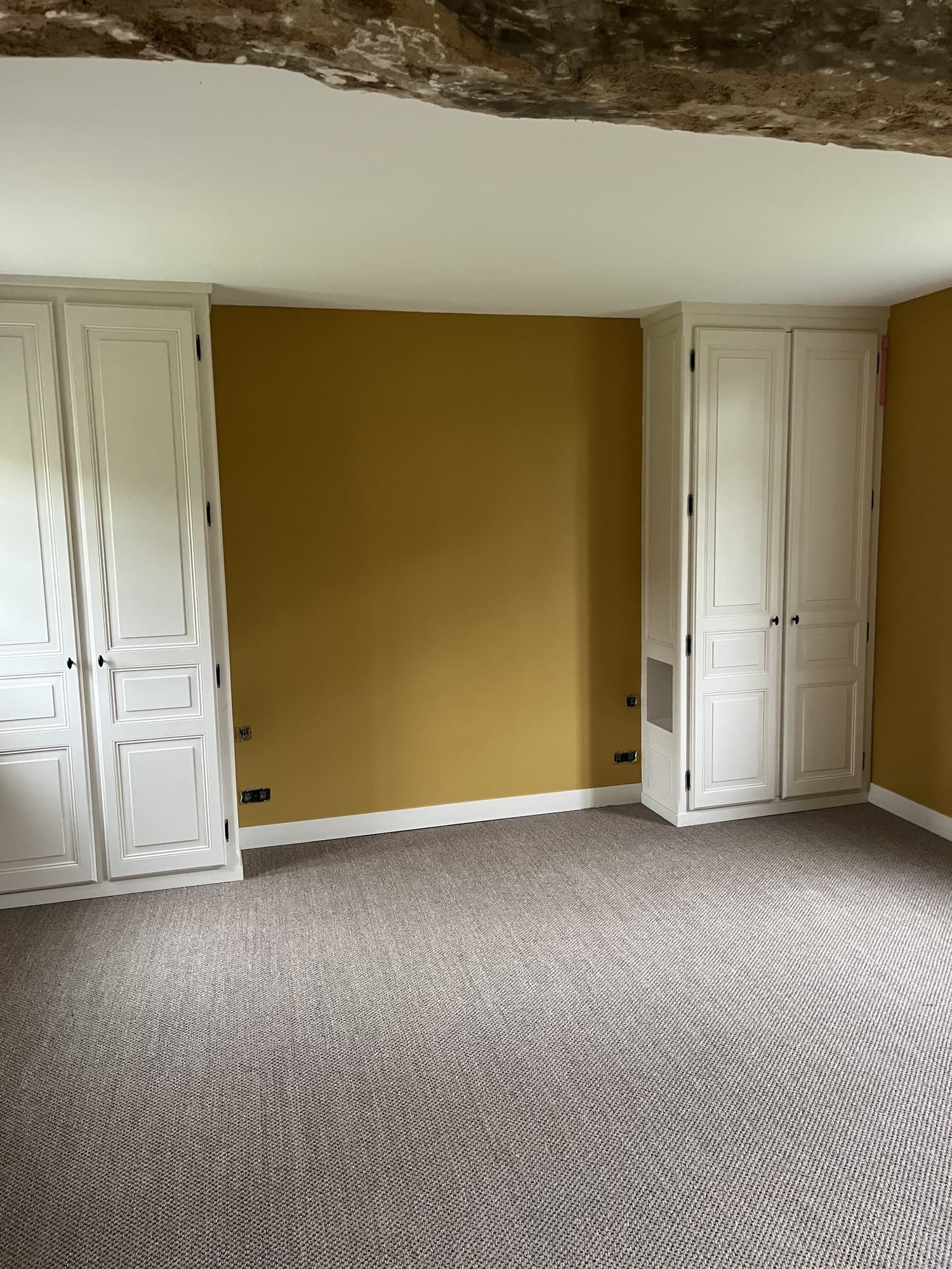 Chambre aux murs ocre, placards à panneaux peints en blanc et poutre apparente