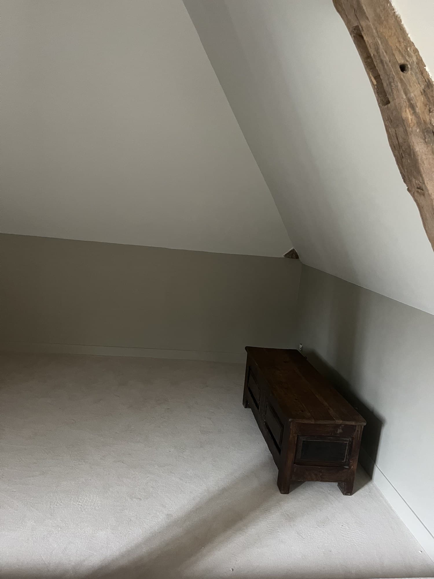 Angle de comble : poutre ancienne apparente contre un mur gris clair mat