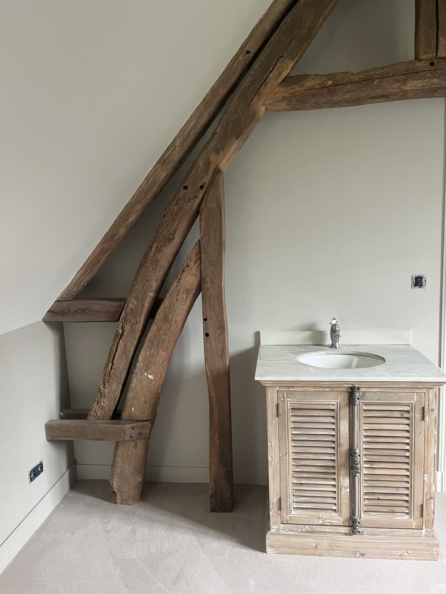 Coin toilette sous charpente : vasque sur meuble en bois clair, poutres anciennes laissées brutes
