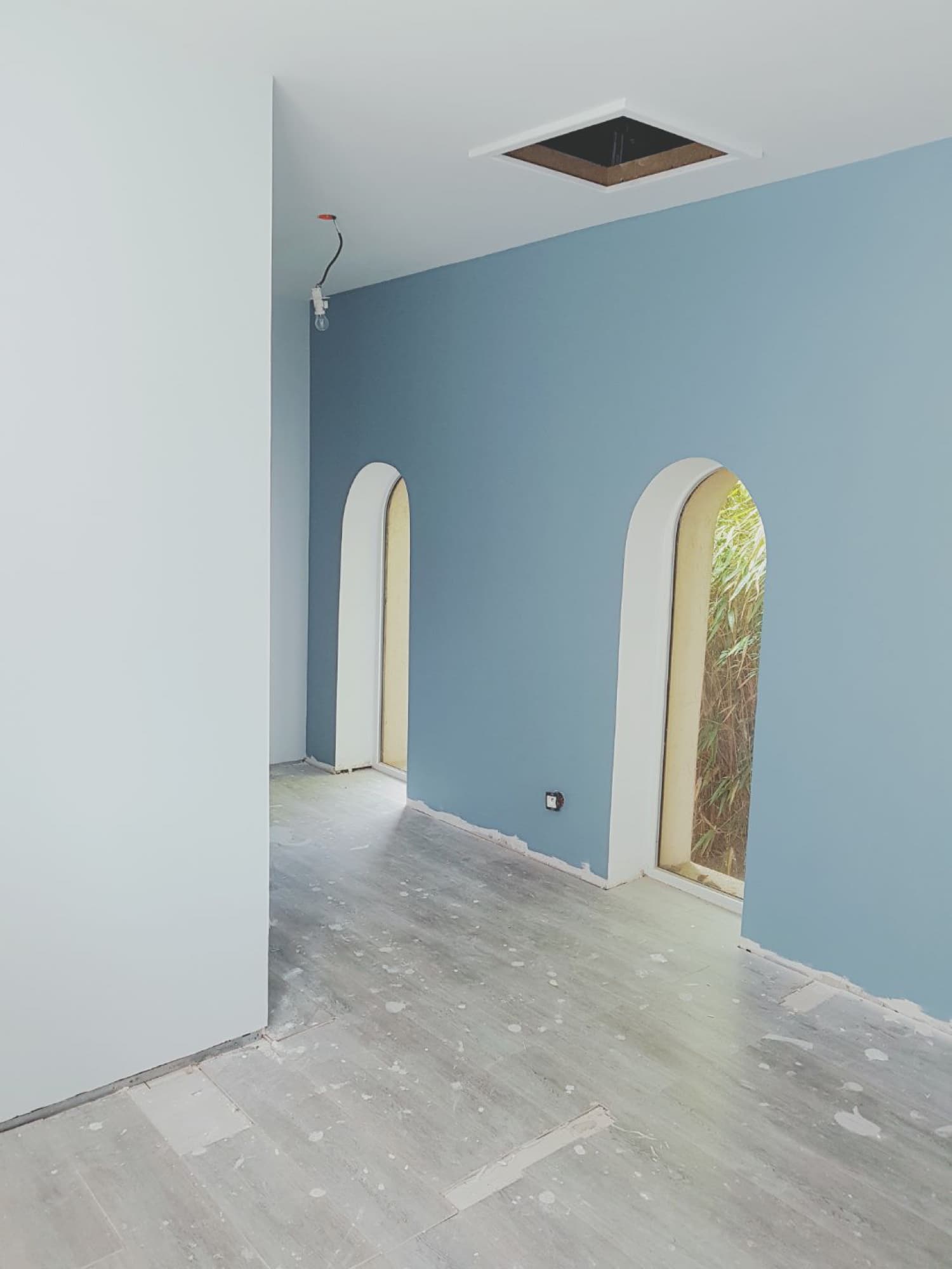 Pièce peinte en bleu-gris profond, deux ouvertures en arche sur le jardin