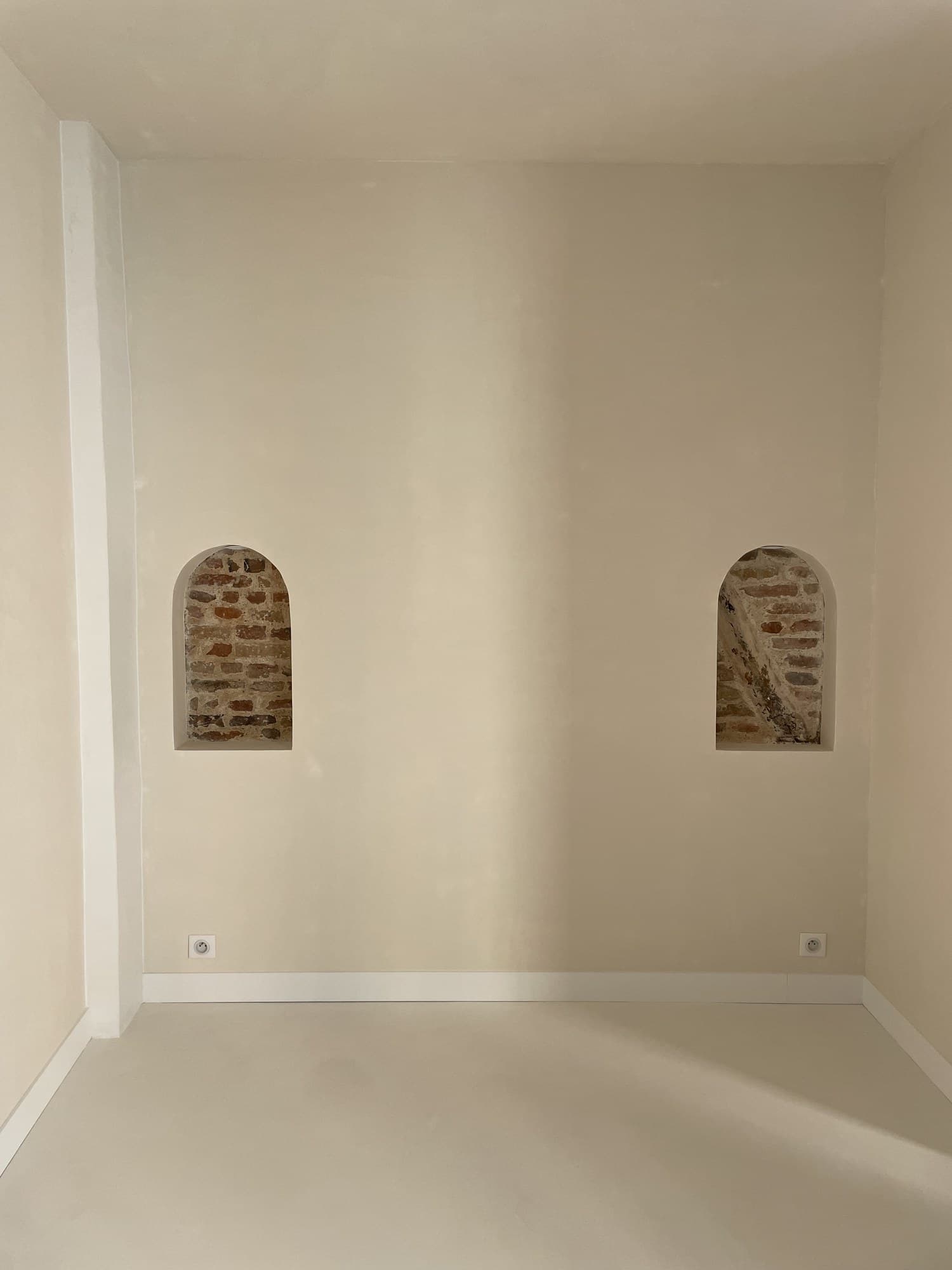 Mur en enduit crème percé de deux niches voûtées en brique apparente